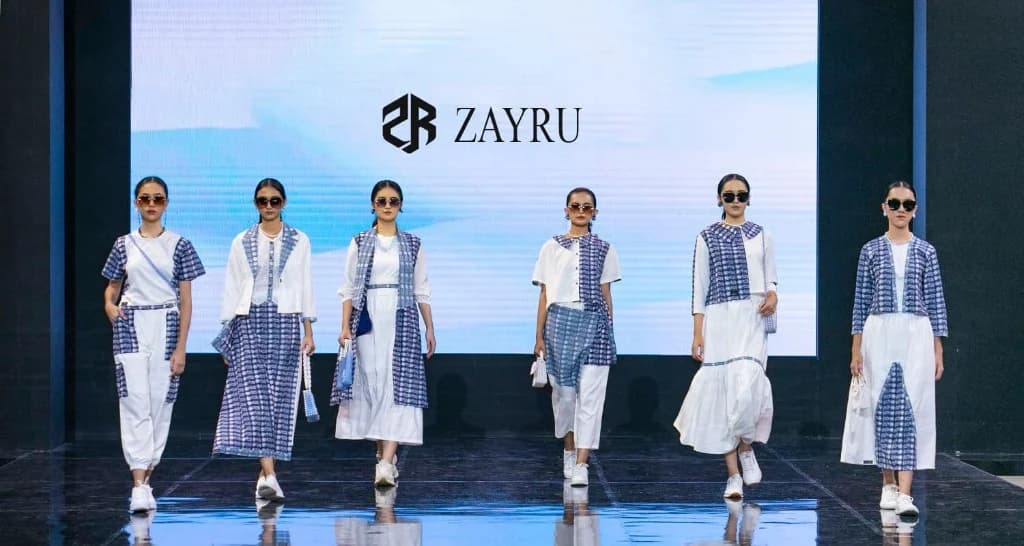 Zayru showcase at Jogja Fashion Week — designer takes the stage between seven models in earthy red and green aksara batik, JFW × Zayru logo lit on the LED backdrop.